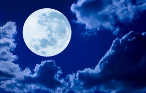 A picture of a full moon, up in the sky, surrounded by clouds.